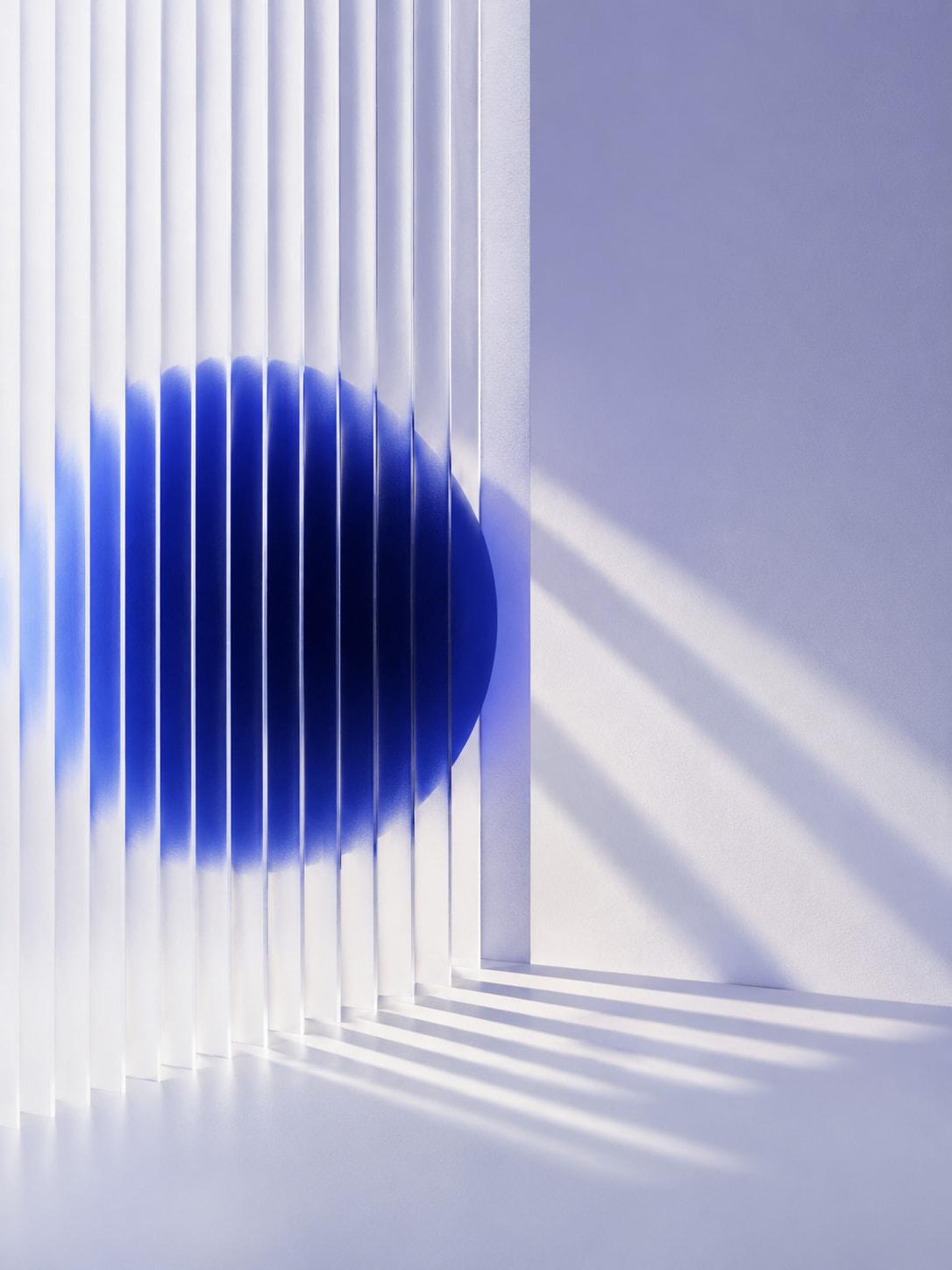 A deep blue sphere seen through fluted glass, broken into vertical bands and throwing striped shadows on the wall.